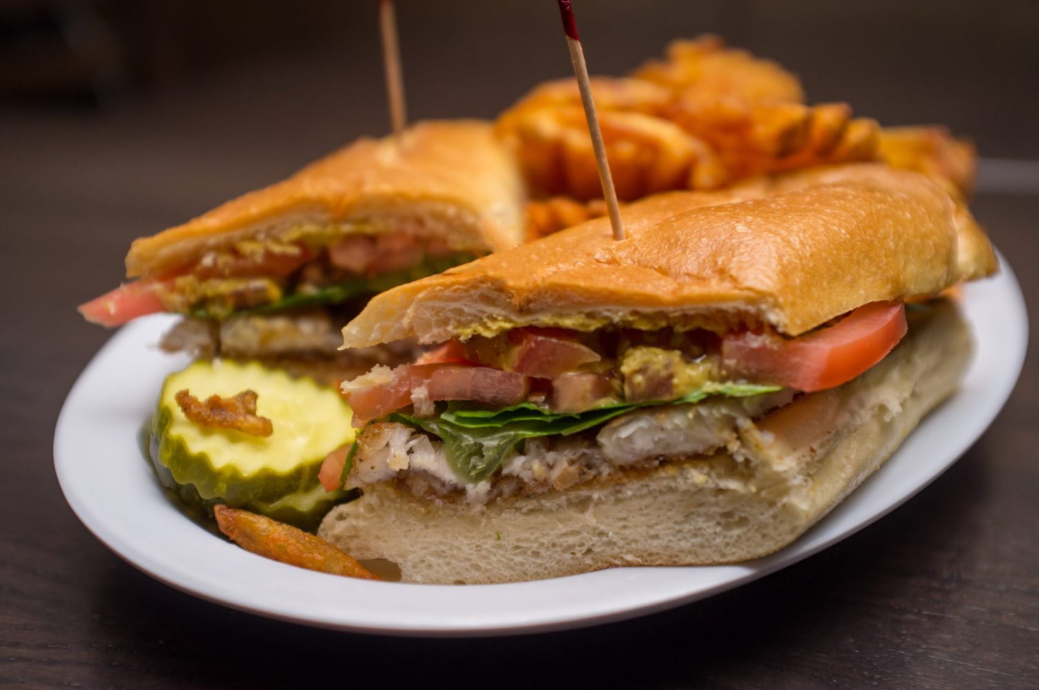 Louisiana codfish po boy on a torpedo roll with pickles and fries